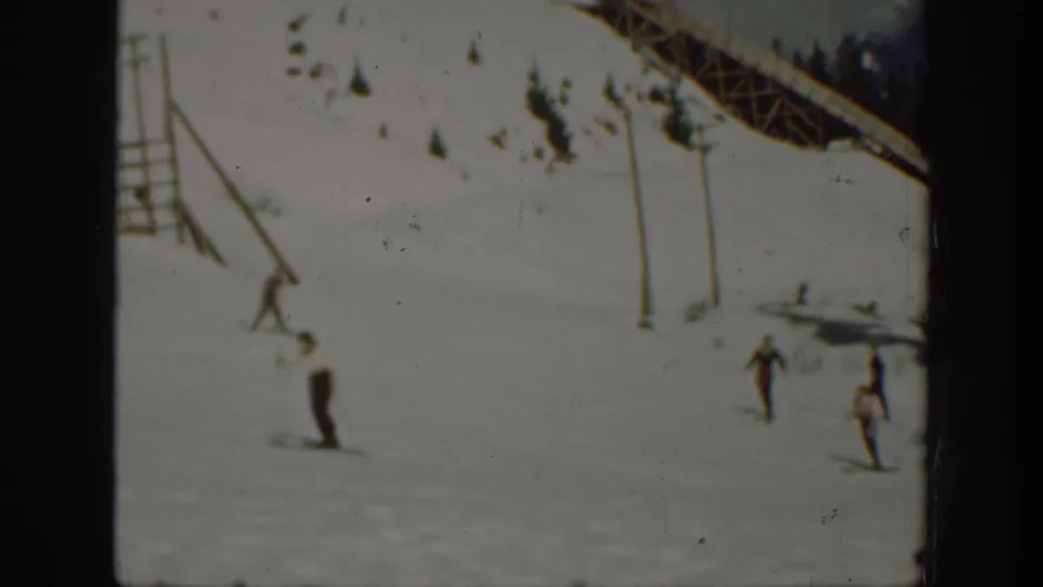 1940 Washington home-movie frame showing distant skiers moving down a snowy slope beneath a lift or trestle structure.