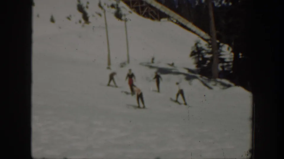 1940 Washington home-movie frame of skiers descending a broad snowy slope with trees and lift supports nearby.