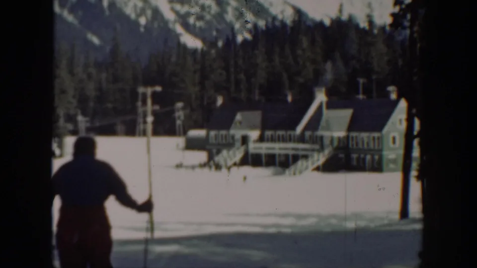 1940 Washington frame showing a skier with poles in the foreground, with a snow-covered lodge, trees, and mountains beyond.