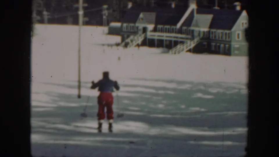 Final 1940 Washington 8mm frame with the skier smaller in the snowfield, lodge buildings beyond, and forested mountain backdrop.