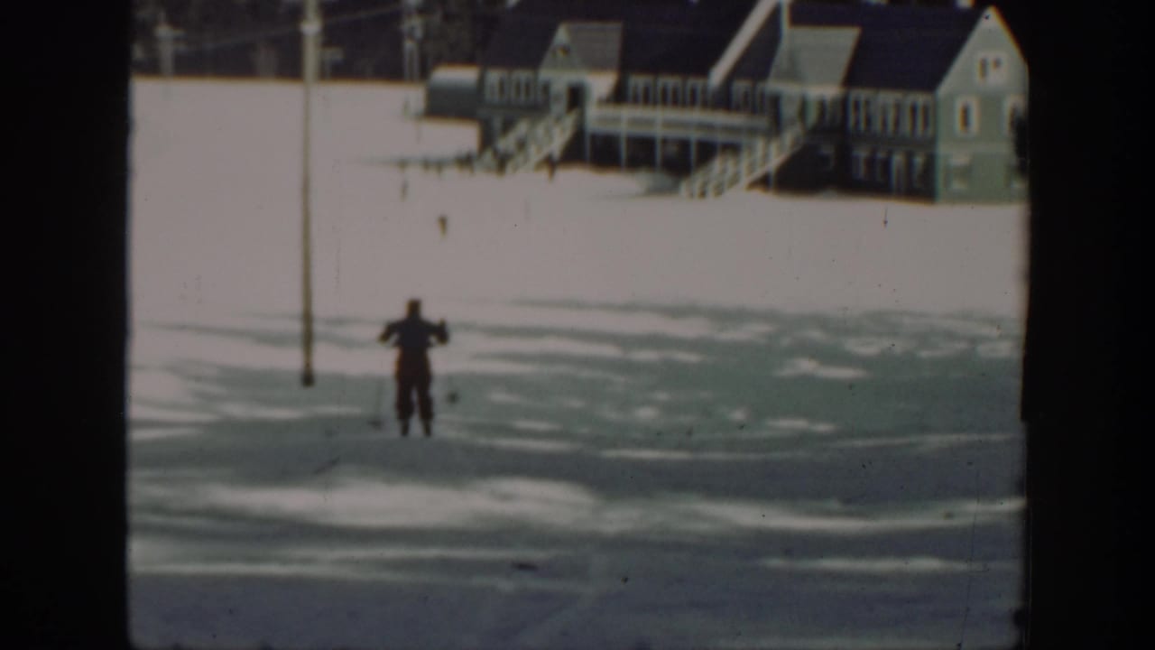A distant skier glides across a snowy Washington landscape with porch-front wooden buildings in the background.
