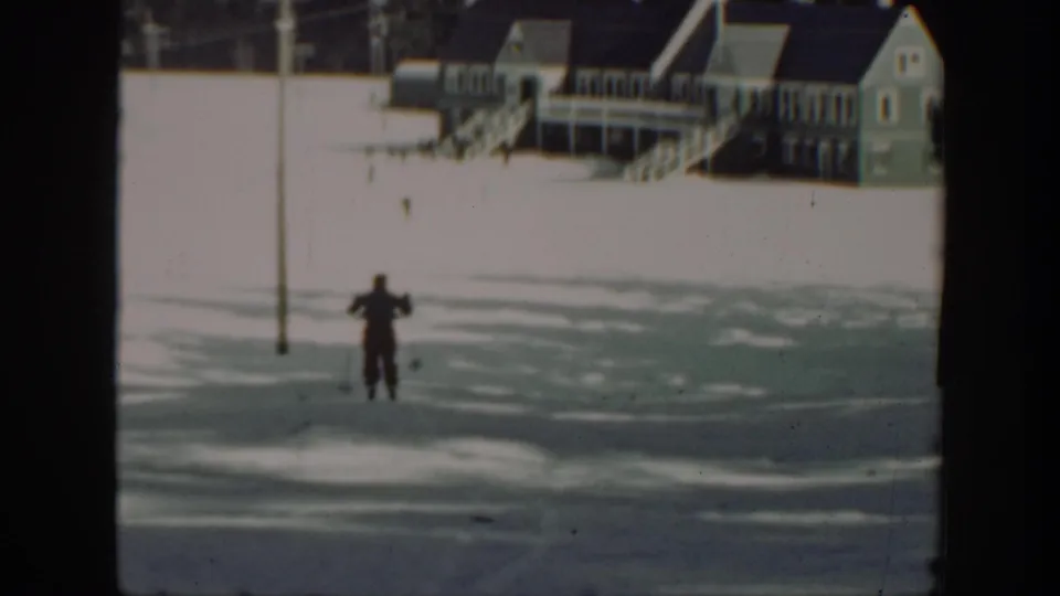 A distant skier glides across a snowy Washington landscape with porch-front wooden buildings in the background.