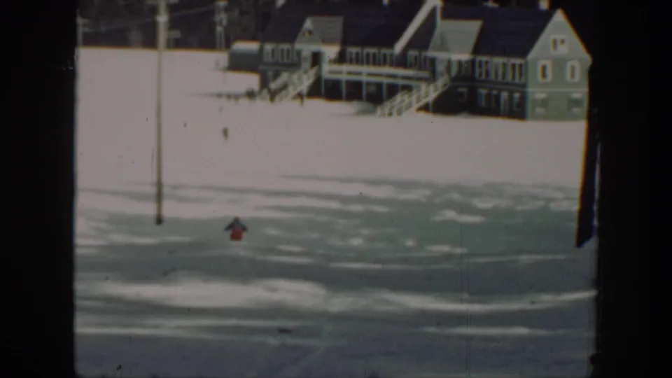 At the end of the clip, the skier appears low in the snowy frame beneath porch-front buildings and a utility pole.