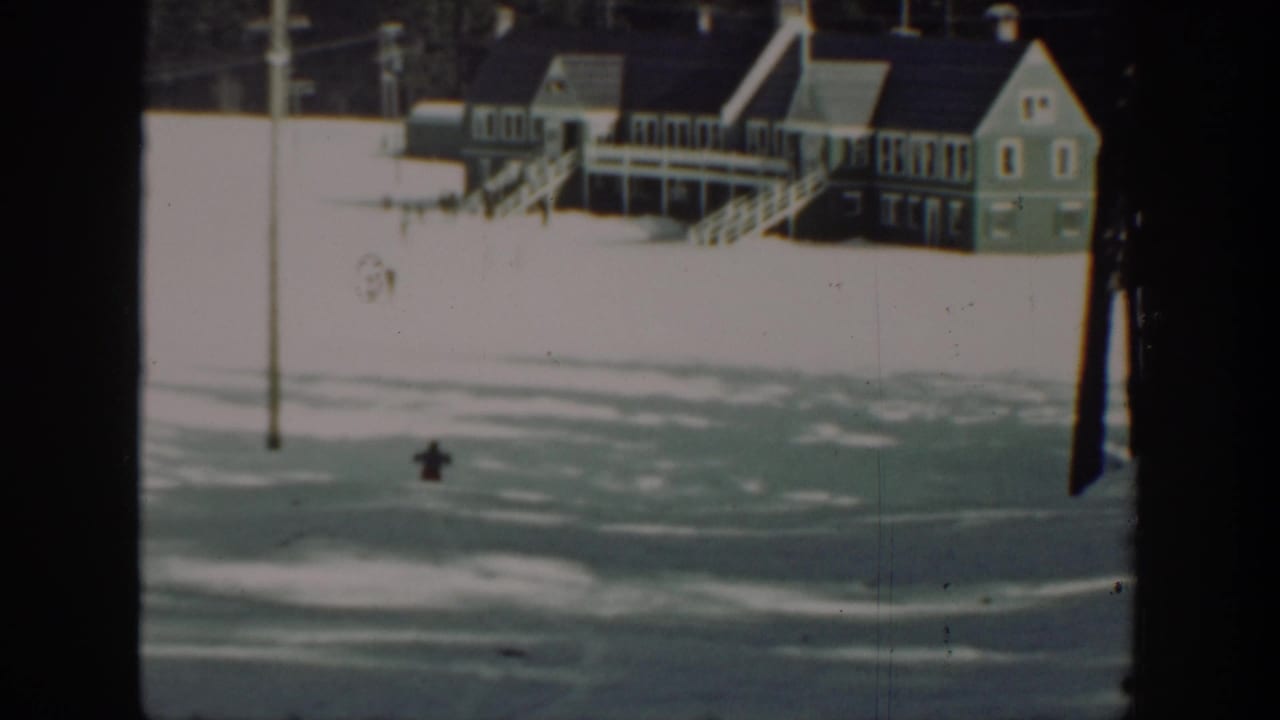 1940s Washington 8mm frame with a small skier crossing a snowy slope beneath a lodge-like building and utility pole.