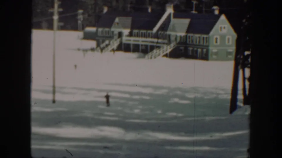 A distant skier moves over the snowy ground near a lodge-like building in this 1940s Washington home-movie frame.