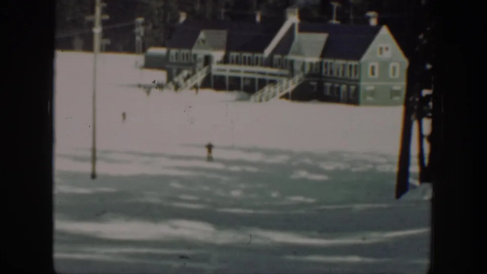 The skier is visible as a small dark figure on a snowy slope beneath a large building with exterior stairs.