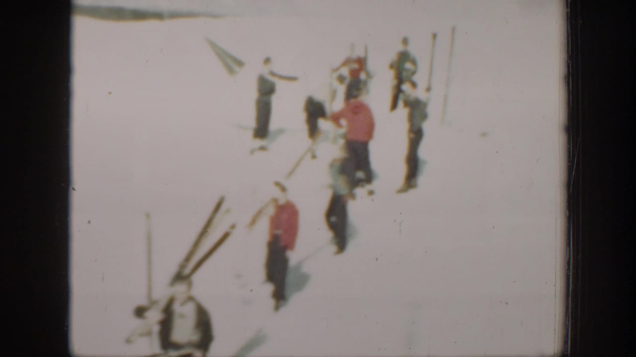 1940 Washington home-movie frame showing several skiers on bright snow, with long wooden skis and poles arranged nearby.