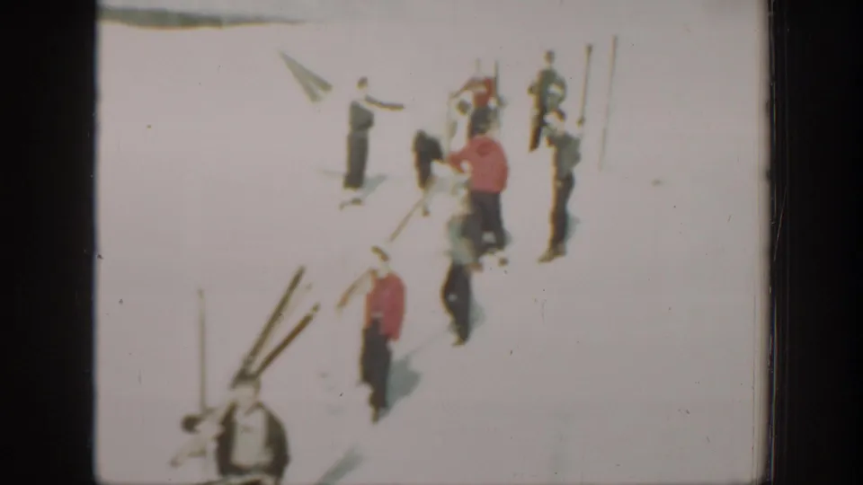 1940 Washington home-movie frame showing several skiers on bright snow, with long wooden skis and poles arranged nearby.