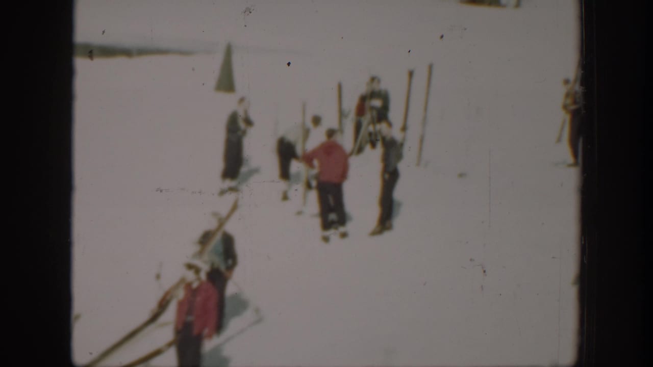 Small groups of skiers stand among skis and poles on snow.