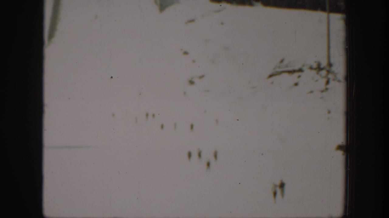 Soft 8mm frame from Washington footage showing a bright snowfield with indistinct distant marks or possible figures.