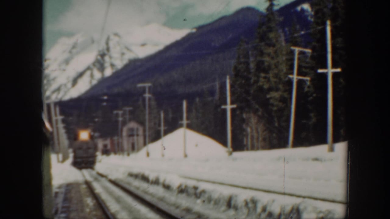 A 1940 Washington 8mm frame shows a distant steam locomotive approaching through snowbanks with forest and mountains behind it.