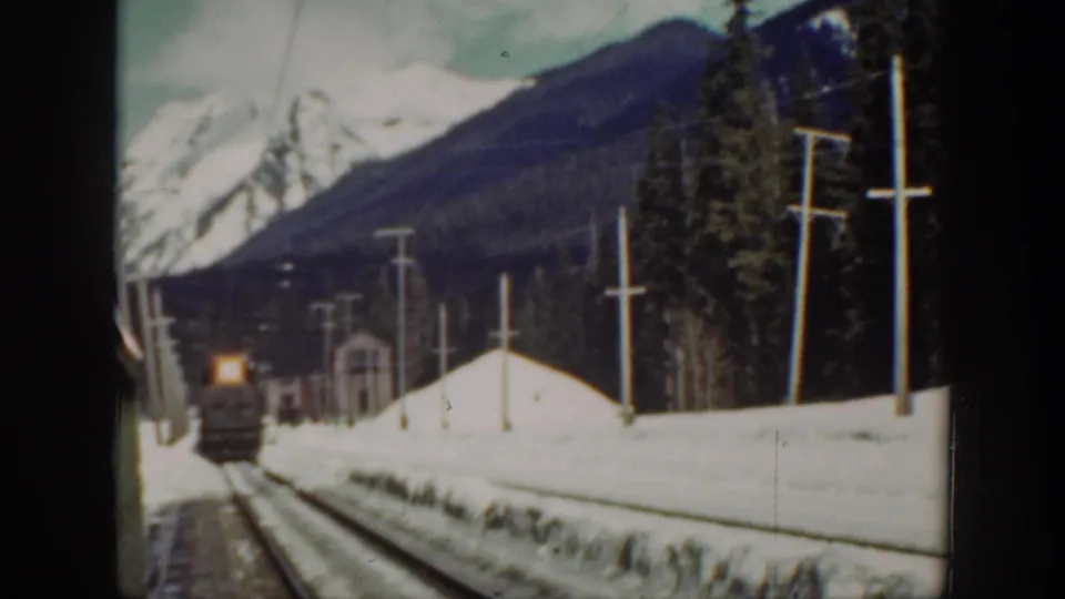 A 1940 Washington 8mm frame shows a distant steam locomotive approaching through snowbanks with forest and mountains behind it.