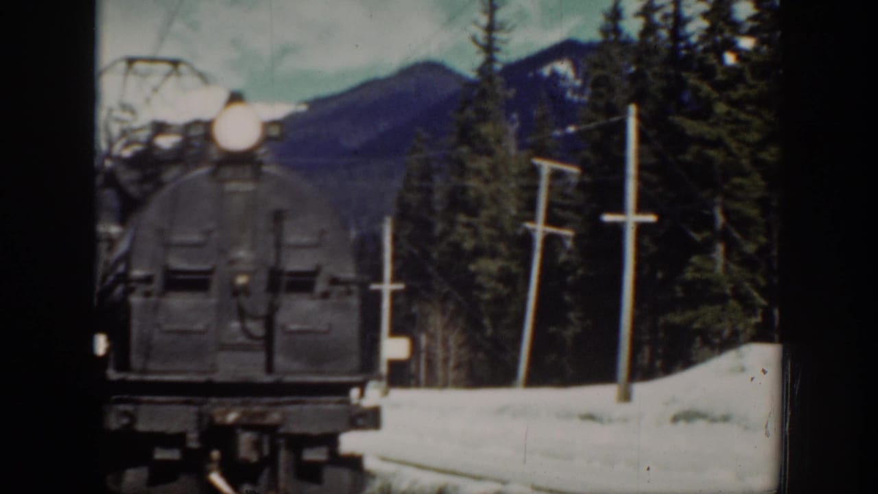 Front of a dark steam locomotive nears the camera on snow-lined rails.