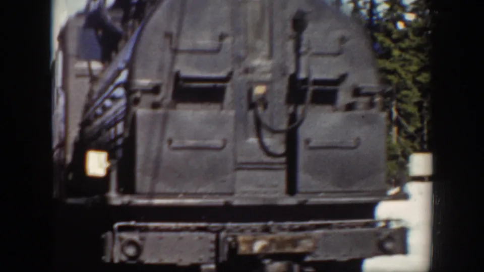A close 8mm view captures the black steam locomotive front as it passes, with metal panels, fittings, and a small lit headlamp visible.