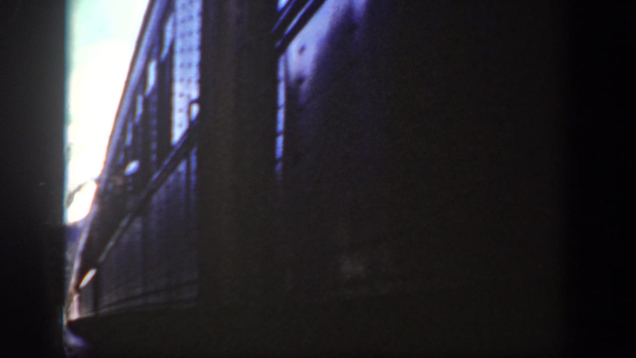 Shadowed side of a train car with windows and a bright opening at the edge.