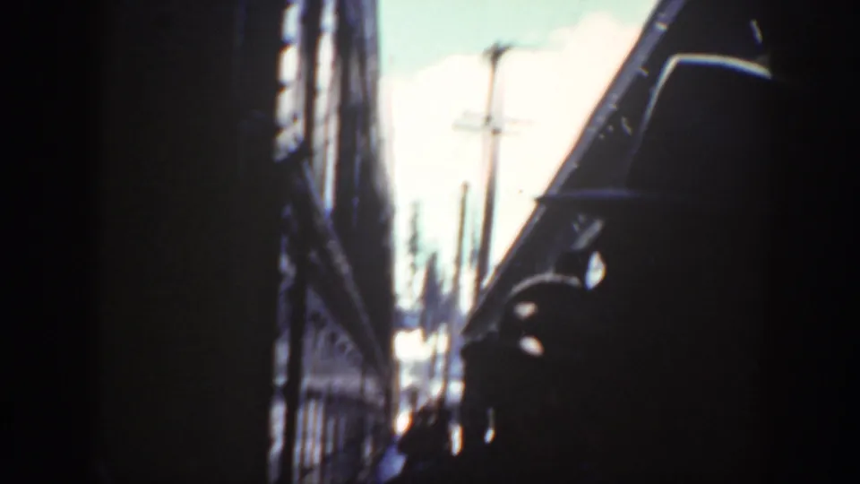 1940 Washington home-movie frame looking through a narrow rail-side passage, with dark silhouettes, utility poles, and blown-out daylight.