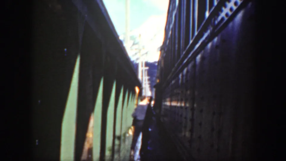 A pedestrian in light clothing moves along a narrow rail-side walkway in Washington, with strong contrast and 8mm color grain.