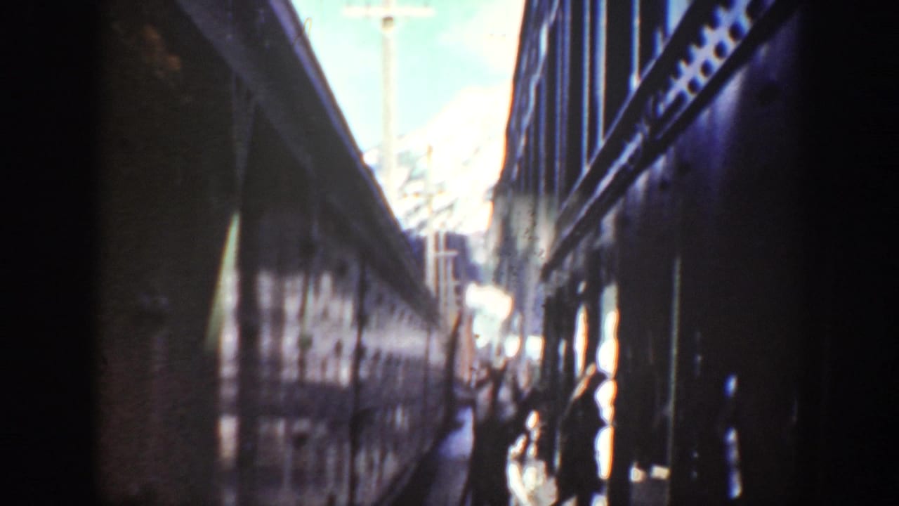Dark train cars frame a bright outdoor gap with figures near the far end.