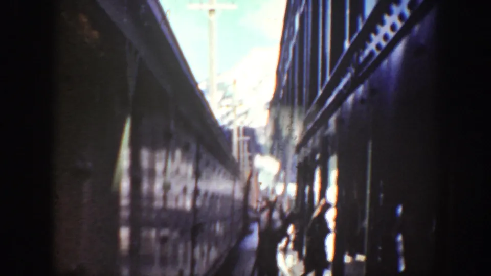 Washington 1940 frame looking down a shadowed gap between rail cars toward bright daylight and small human figures.
