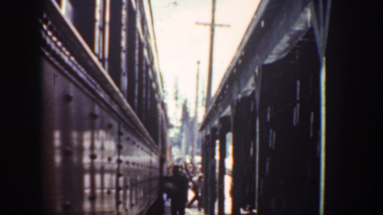 Narrow passage between two dark structures with distant people under a bright sky.