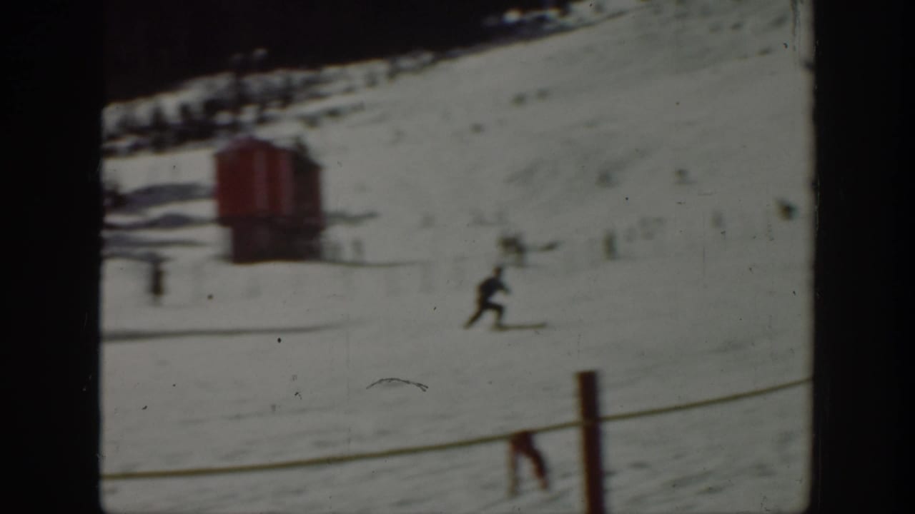1940 Washington 8mm frame showing a skier crossing a snow-covered mountain slope with a red lift or slope structure nearby.