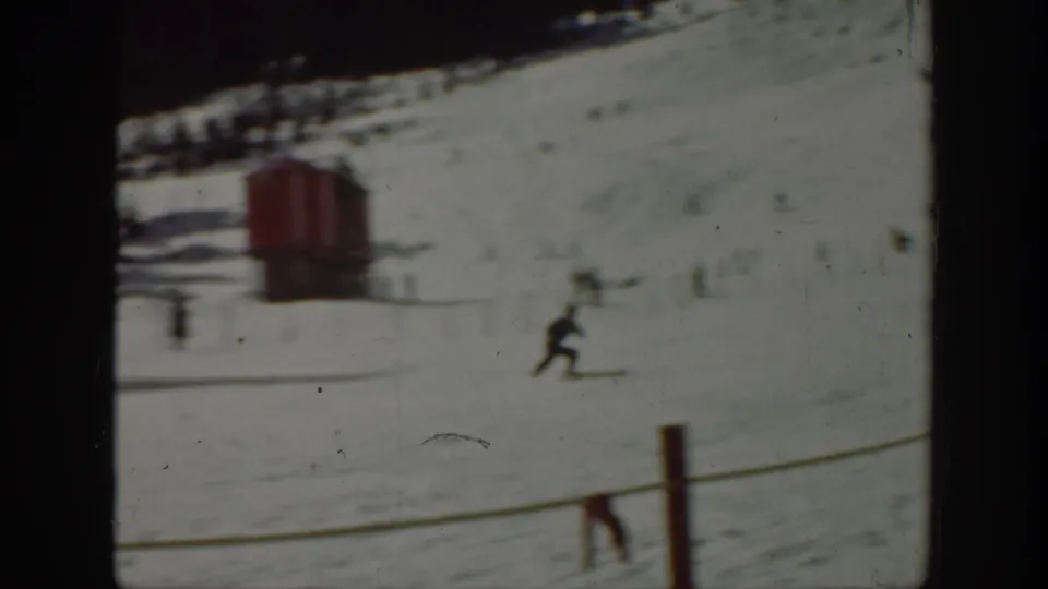 1940 Washington 8mm frame showing a skier crossing a snow-covered mountain slope with a red lift or slope structure nearby.