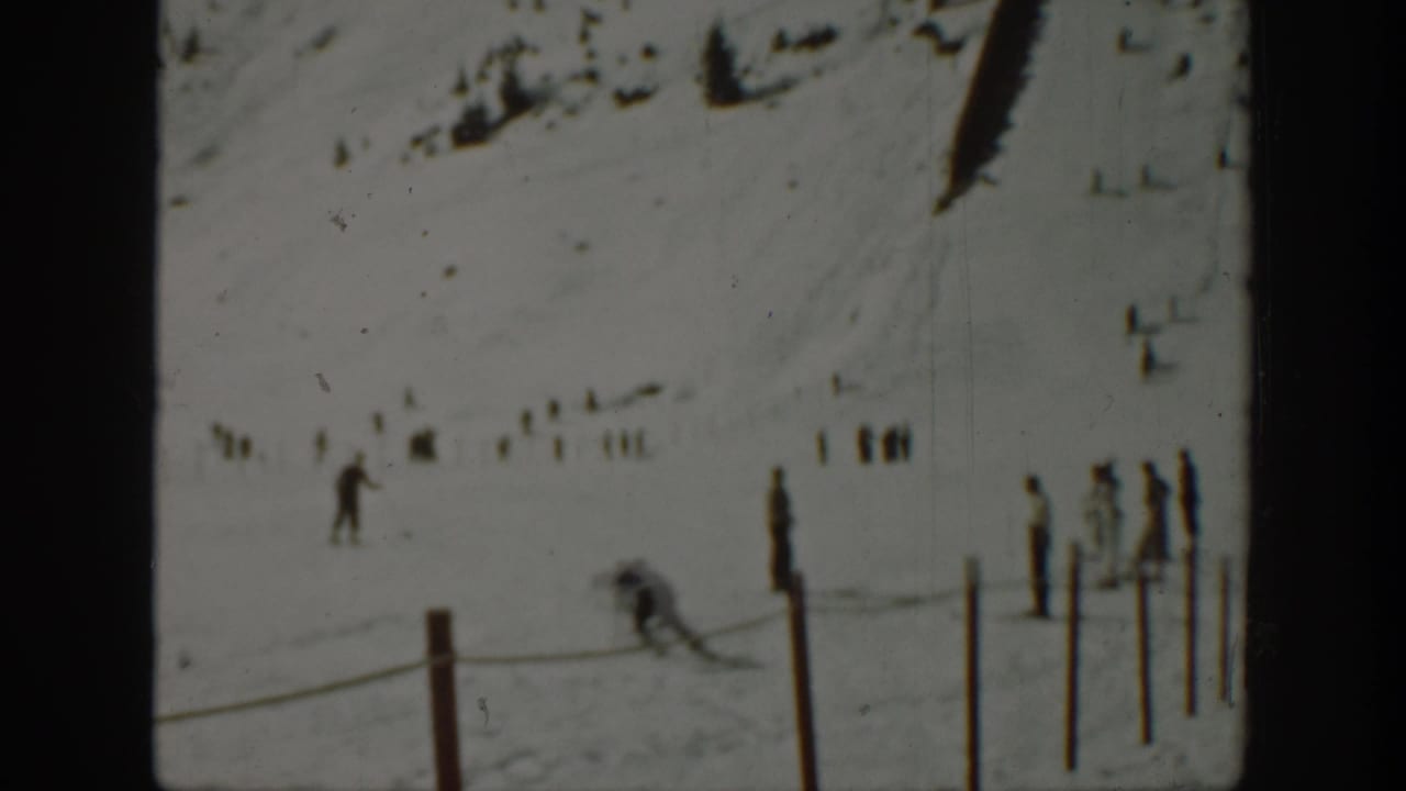 1940 Washington 8mm frame with distant skiers and spectators spread across a snow-covered mountain slope behind a rope line.