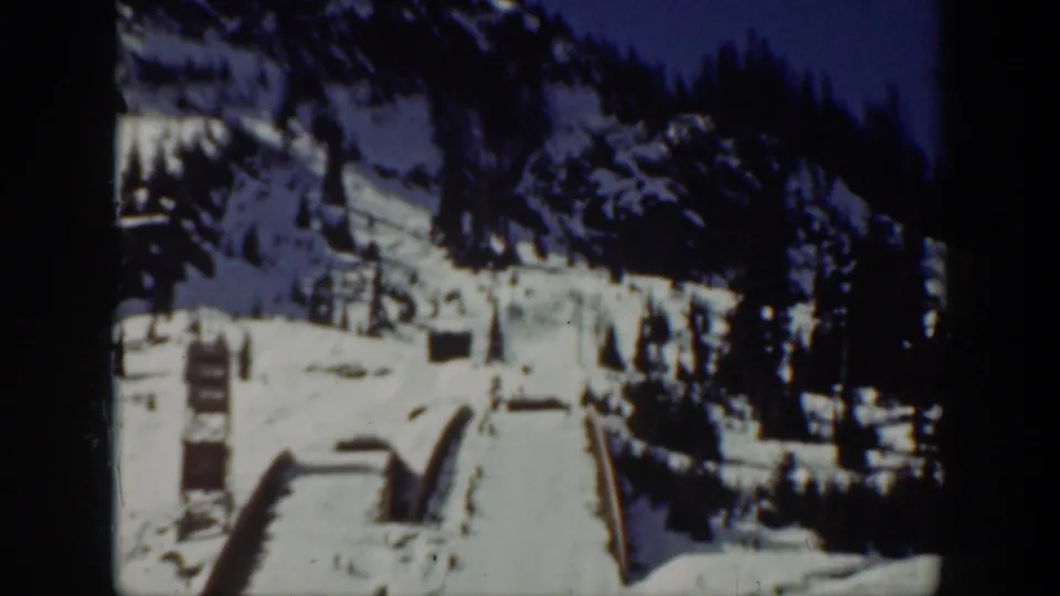 1940 Washington 8mm frame showing a snowy mountain ski area with pine trees, slope structures, and distant people.