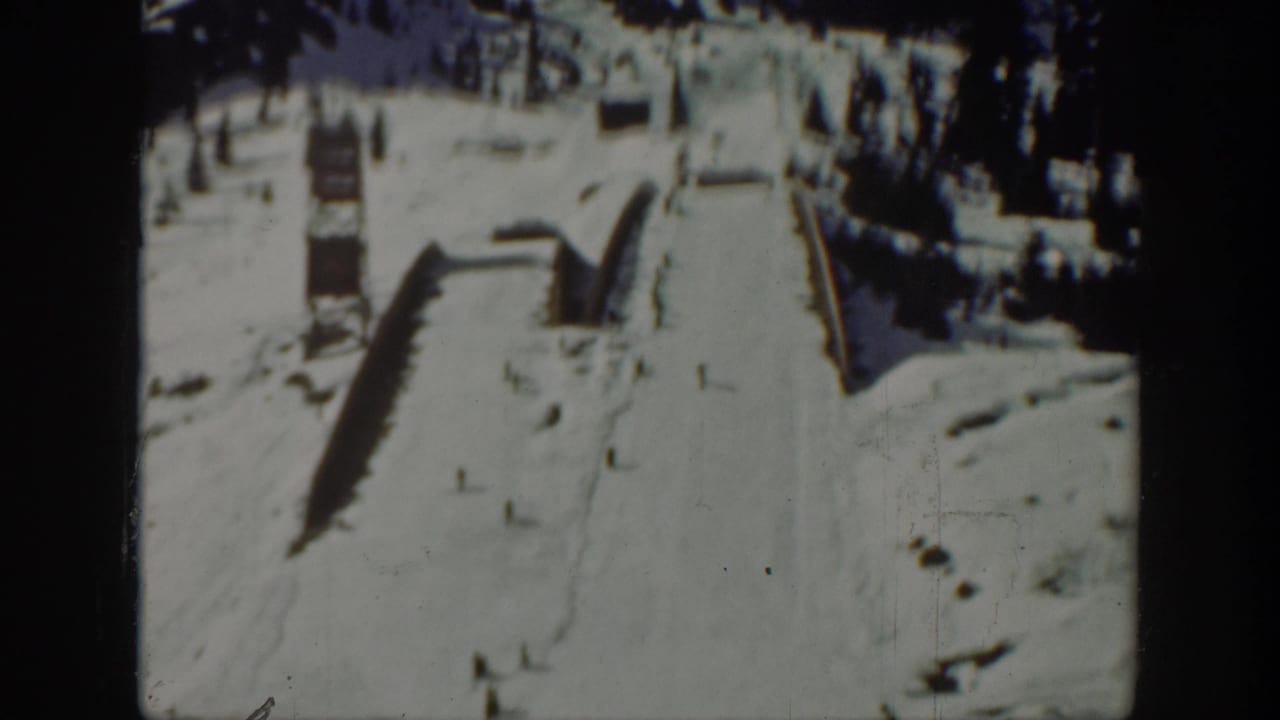 1940 Washington frame of a snowy ski slope with simple wooden ramp features and dark evergreen trees above.