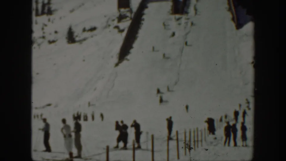 1940 Washington frame showing spectators along the lower edge of a snowy ski slope with wooden structures uphill.