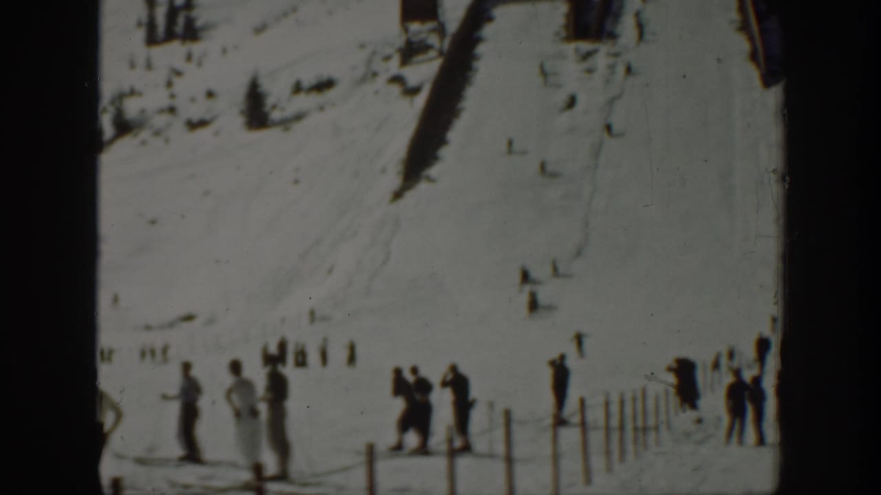 Washington 1940 home-movie frame showing skiers gathered near a fence below a snowy mountain slope.