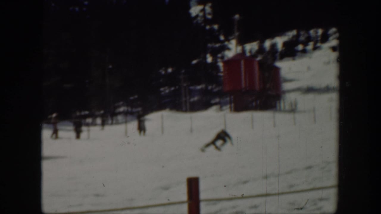 1940 Washington home-movie frame showing a distant skier on a snow-covered slope near a red lift or tow structure.