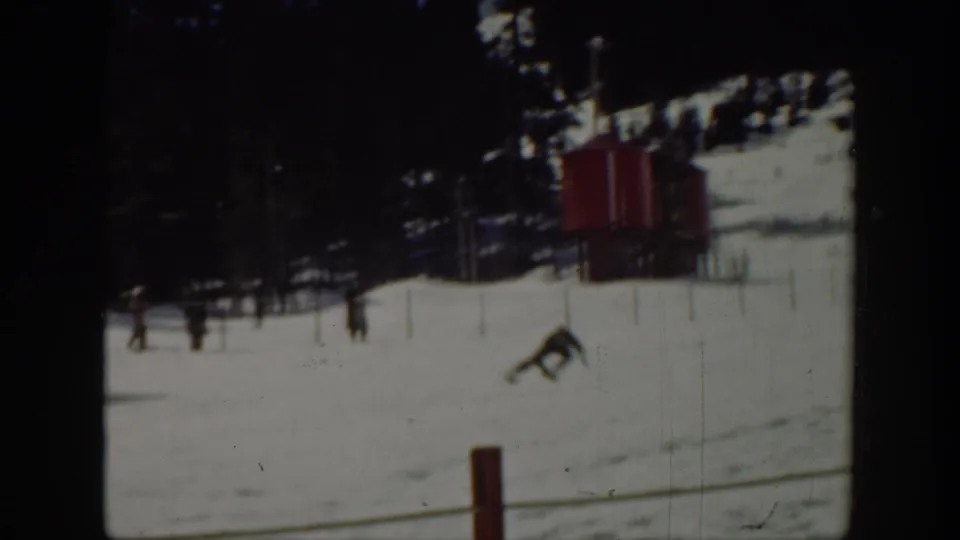1940 Washington home-movie frame showing a distant skier on a snow-covered slope near a red lift or tow structure.