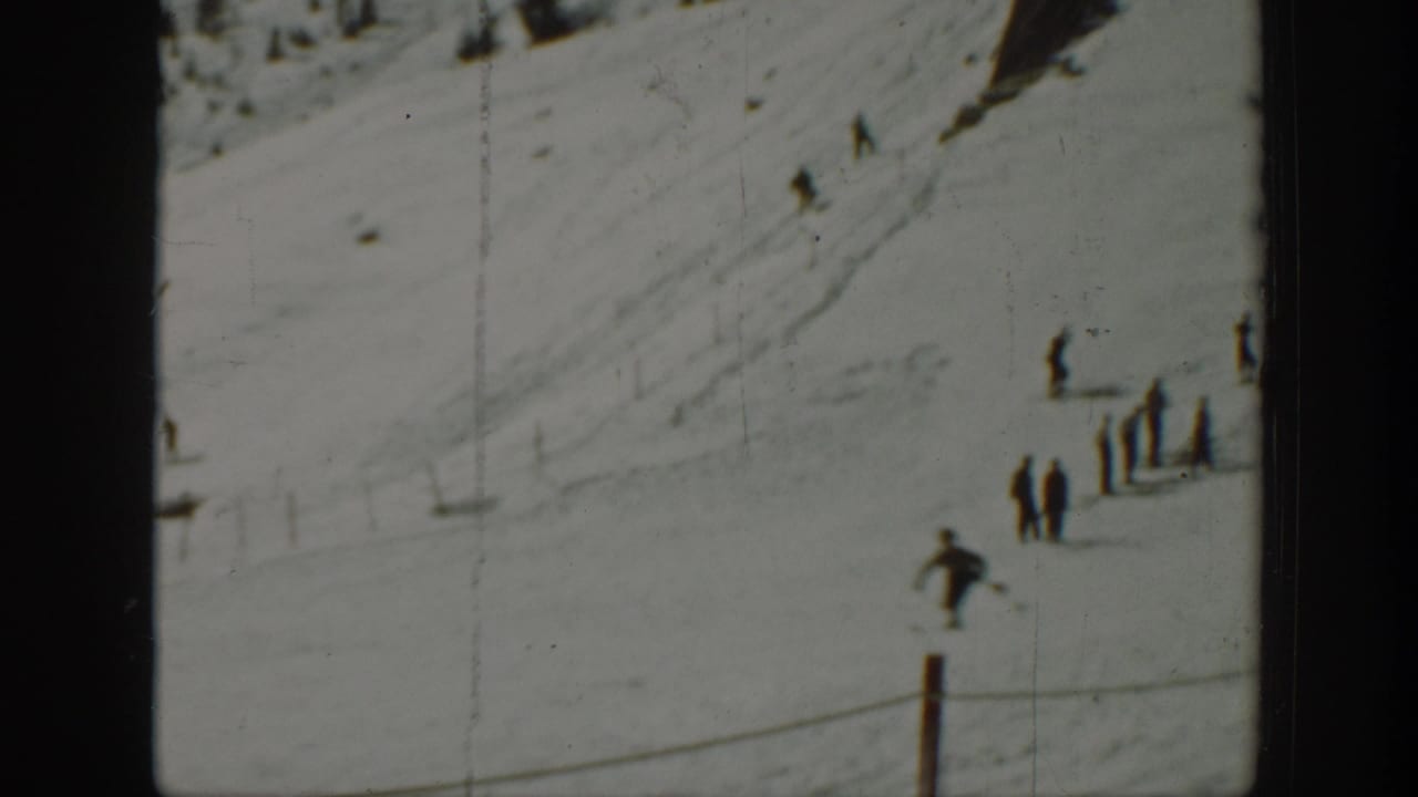 Wide snowy slope with several distant skiers and a rope or fence line.