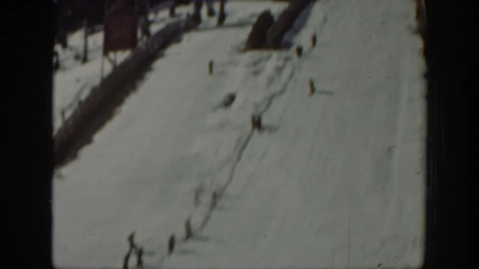 Distant skiers move across a snowy hillside in Washington 1940 home-movie footage, with dark tree edges and soft 8mm focus.