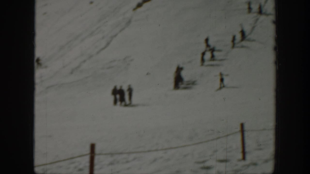 Small figures stand and ski on an open snowy slope.
