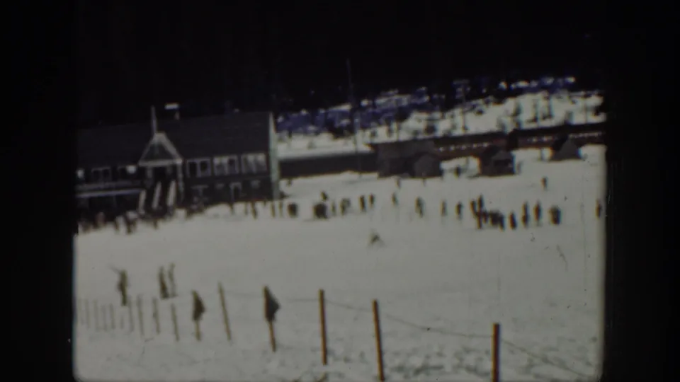 1940 Washington 8mm frame with distant skiers on snow, a large wooden lodge at left, fence posts in front, and forest in the background.