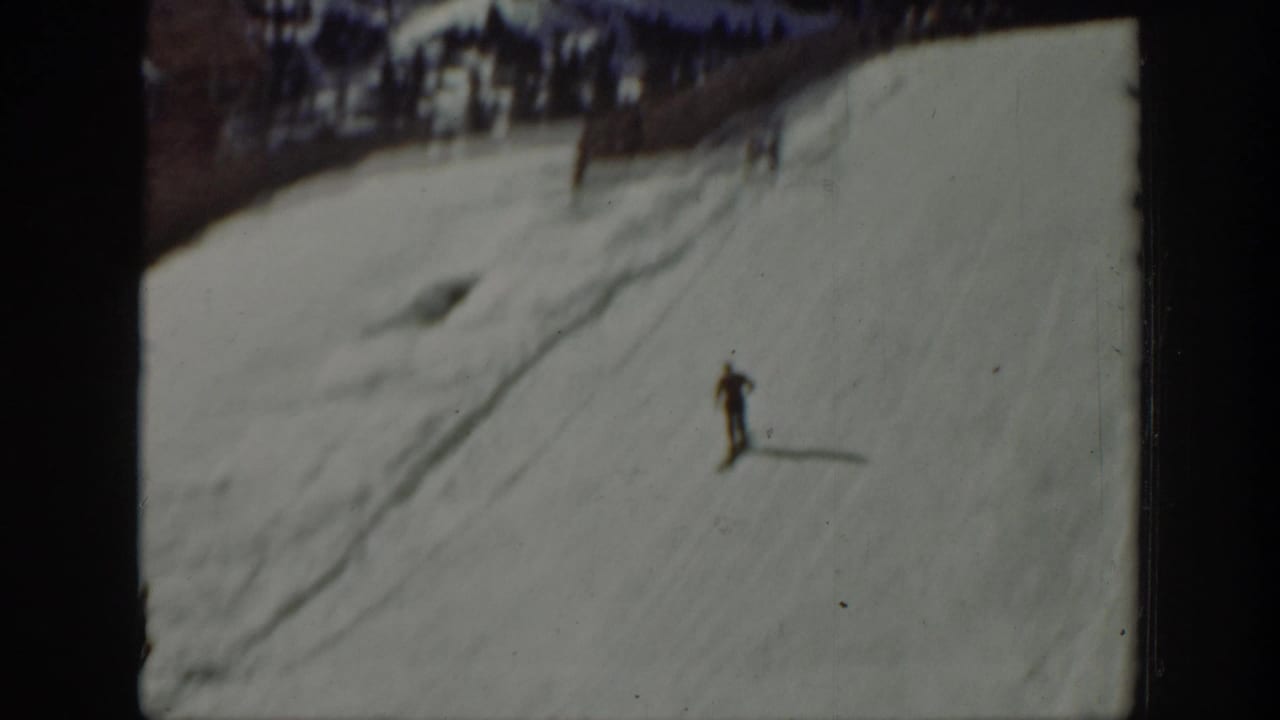 Single skier descending a broad snowy slope with tracks in the snow.