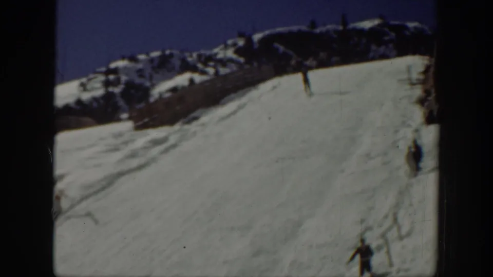 1940 Washington home-movie frame of skiers on a snow-covered slope near the wooden ramp area below a rocky ridge.