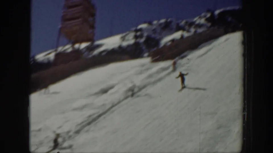 1940 Washington home-movie frame showing a skier on an open snowy slope, with ridge line and a partial vertical structure at the edge.