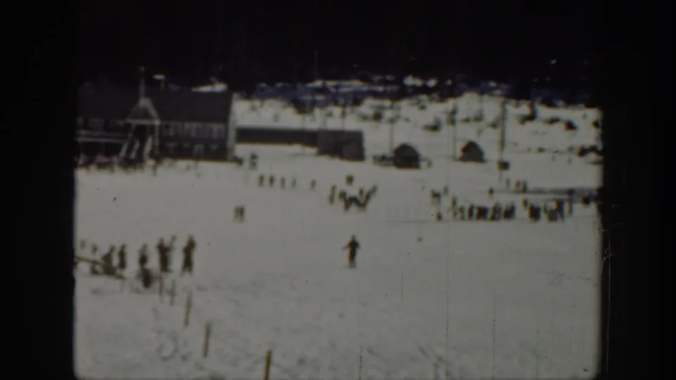 1940 Washington ski-area frame showing distant people on snow near lodge-like buildings at the base of the slope.