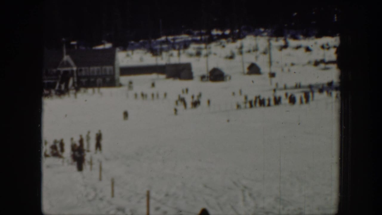 1940 Washington home-movie frame showing a snowy ski area, distant spectators, and a lodge-like structure near the slope.