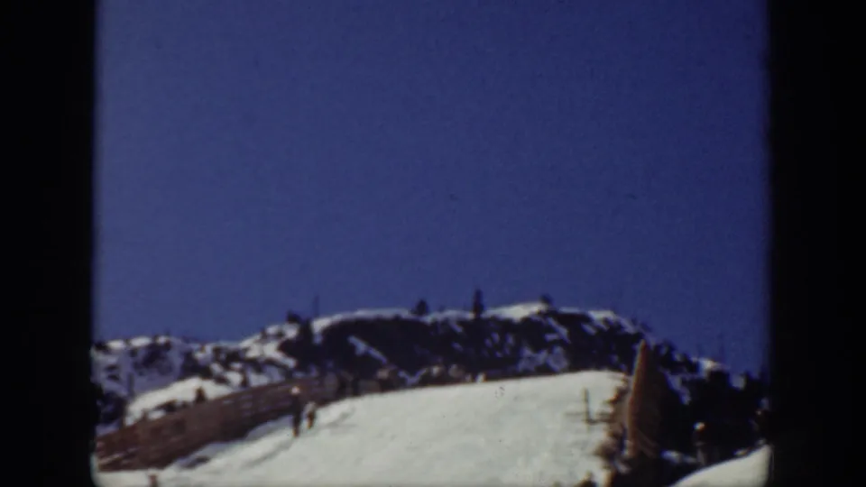 Color frame from the Washington ski resort footage showing a fenced snowy slope, ridge line, and small figures beneath a blue sky.