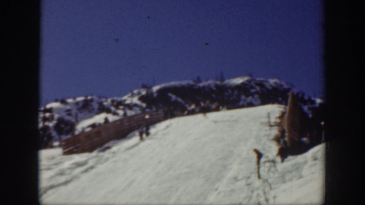 1940 Washington ski-area frame with a broad snow run, distant ridge, fence line, and a small skier standing or moving at the right edge.