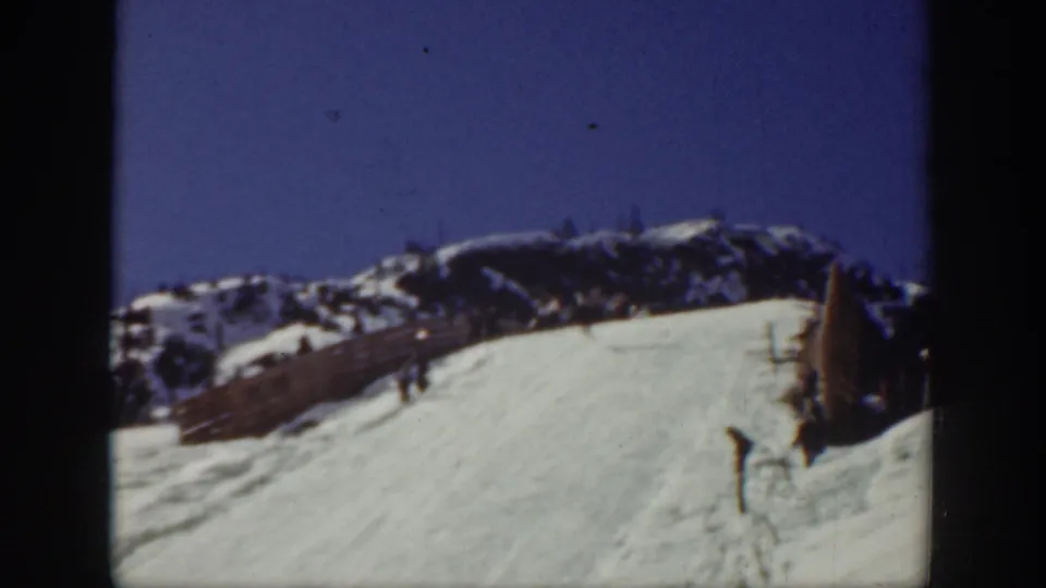 1940 Washington ski-area frame with a broad snow run, distant ridge, fence line, and a small skier standing or moving at the right edge.