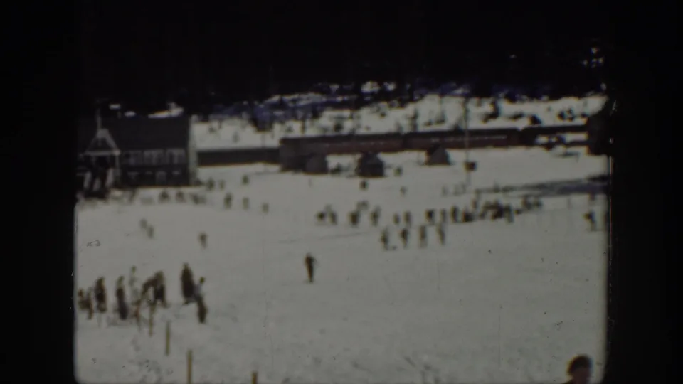 1940 Washington ski-area frame showing a snowy base area with a lodge-like building, dark tree line, and scattered visitors or skiers.