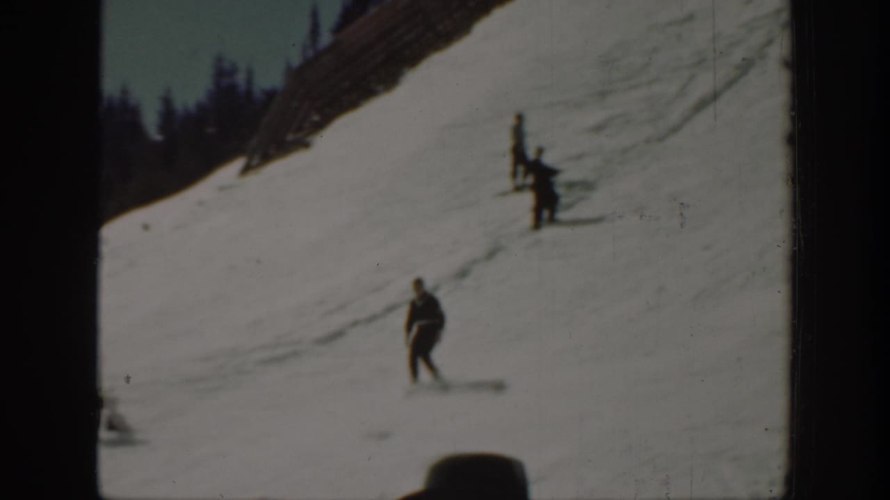 1940 Washington home-movie frame showing men moving across a snowy mountain slope below a dark evergreen treeline.