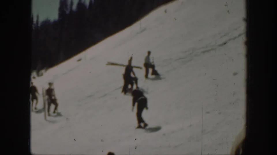 1940 Washington home-movie frame with men on a snowy hillside, one bent forward as if skiing or walking downhill.