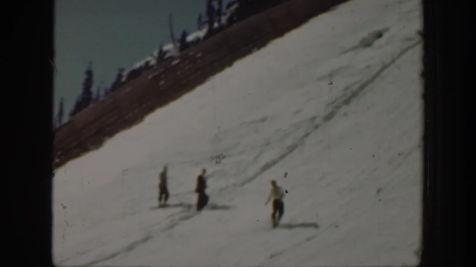 1940 Washington 8mm frame showing distant men spaced across a bright snowy hillside under a dark evergreen ridge.