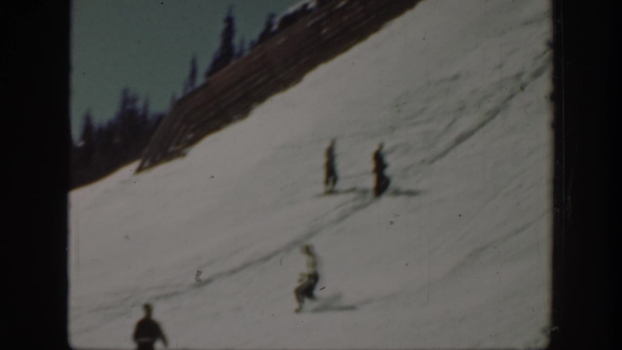 1940 Washington home-movie frame showing distant skiers on a snowy hillside with a fence and dark evergreens above.